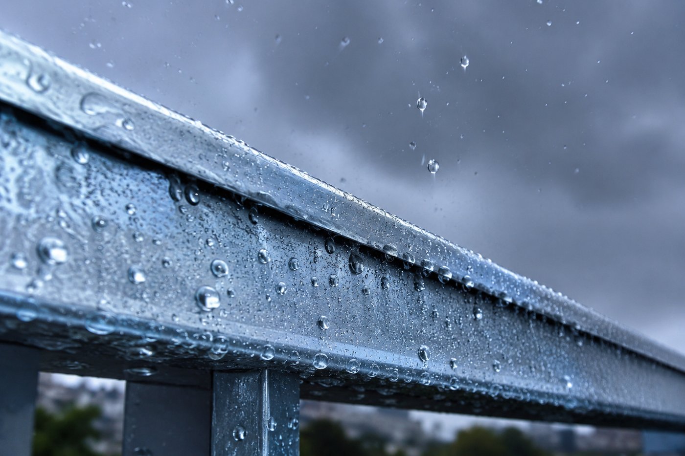 Viga de aço galvanizada sob chuva, com gotas de água acumuladas em pérolas sobre a superfície zincada azulada e brilhante